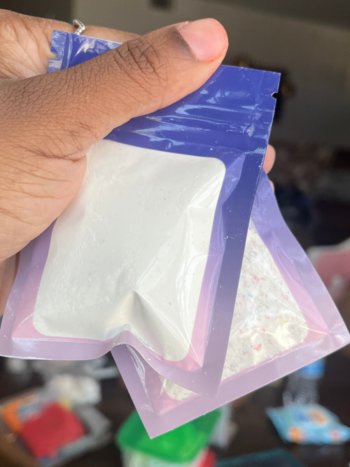 Hand holding a small plastic bag with a white substance against a blurred indoor background